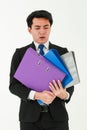 A young tired employee holding a stack of heavy folders, looking unhappy on his face and suffering from overloaded work, on white