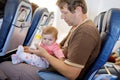 Young tired father and his crying baby daughter during flight on airplane going on vacations