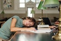 Young tired female student sleeping on desk with books around during study in library of university Royalty Free Stock Photo