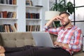 Young tired freelancer in casualwear sitting on sofa in front of laptop