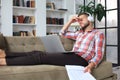 Young tired freelancer in casualwear sitting on sofa in front of laptop