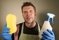 Young tired and frustrated single man or house husband cleaning with detergent spray and sponge stressed and exhausted as domestic