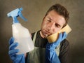 Young tired and frustrated single man or house husband cleaning with detergent spray and sponge stressed and exhausted as domestic