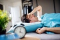 Young tired man with alarm clock in bed at home, waking up in morning. Royalty Free Stock Photo