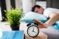 Young tired man hitting alarm clock in bed at home, waking up in morning. Royalty Free Stock Photo