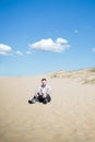 Young tired man sitting on the top of sand dune in desert, sand is al around and some greens. Hot summer weather, concept of trave Royalty Free Stock Photo