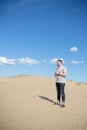 Young tired man standing with bottle water while sitting on the top of sand dune in desert, sand is al around and some greens. Hot Royalty Free Stock Photo