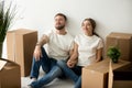 Young tired satisfied couple relaxing on floor with moving boxes