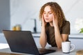 Young tired woman sitting in front of laptop while touching her forehead during work over project Royalty Free Stock Photo