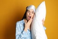 Young tired woman with sleeping mask and pillow yawning on yellow background Royalty Free Stock Photo