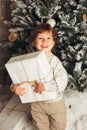 Young toddler Caucasian Boy Holding Christmas Present In Front Of Christmas Tree. Cute happy smiling boy. Vertical photo Royalty Free Stock Photo