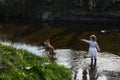 A young toddler girl wading in a river, commanding a dog to fetch.