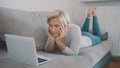 Young toughtful woman chatting with frends on social media using laptop on her couch.