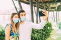 Young tourist couple takes a photo with a medical mask in a green urban background