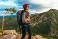 A young tourist girl with a backpack enjoys the sunset from the top of the mountain. Portrait of a traveler in a red riding hood. Royalty Free Stock Photo