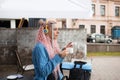 A young tourist girl in a blue shirt drinks coffee and listens to music with headphones. A girl with long pink hair is