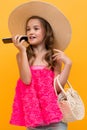 Young tourist girl in a summer pink t-shirt with a straw hat on her head chatting on the phone on a yellow studio Royalty Free Stock Photo