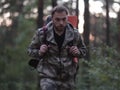 Young tourist man with backpack in camouflage unionalls walking through the forest. Male is engaged in orienteering.