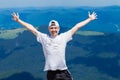 Young tourist man in a cap with hands up on the top of the mountains admires the nature Royalty Free Stock Photo