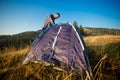 Young tourist man setting up tent on autumn meadow, traveling high in mountains
