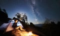 Man resting beside camp, bonfire and tourist tent at night Royalty Free Stock Photo