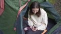 A young tourist sits in a tent in nature and looks at the phone. Surfing the Internet outside the city on hike