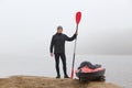 Young tourist in warm clothes stands on bank of river and assembles kayak to travel on icy river under grey sky