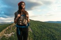 A young tourist woman with a backpack enjoys the sunset from the top of the mountain. Portrait of a traveler in a red riding hood Royalty Free Stock Photo