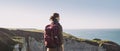 Young tourist woman with backpack looking at sea in Normandy, France over beautiful cliffs background