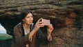 Young tourist woman backpacker photographing landscape on her smartphone camera after hiking on rock at sunset