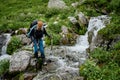 Young tourist woman wades across the mountain river with trekking poles Royalty Free Stock Photo