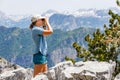 Young tourist woman watching birds in the mountains. Slim hiker birdwatcher girl with binoculars