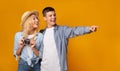 Young tourists holding camera and pointing away over yellow background Royalty Free Stock Photo