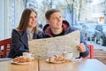 Young tourists man and woman reading map of city in outdoor cafe. Couple drinking coffee tea and eating croissants, spring city Royalty Free Stock Photo