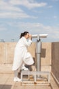 Young toursit woman standing on building tower looking through binoculars telescope Royalty Free Stock Photo