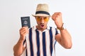 Young tourtist man wearing summer hat and holding USA passport over isolated background annoyed and frustrated shouting with Royalty Free Stock Photo