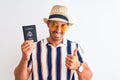 Young tourtist man wearing summer hat and holding USA passport over isolated background happy with big smile doing ok sign, thumb Royalty Free Stock Photo