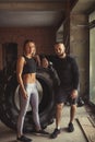 Young trained woman working out with truck tire with personal trainer assistance