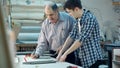 Young trainee studying how to construct a frame, senior worker talking to him behind the desk in frame workshop