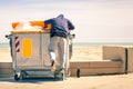 Young tramp rummaging in trash container looking for food and re