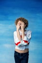 A young transgender guy in a white sweater with a rainbow symbol covered his face with hands