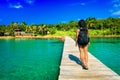 Young travel girl backpacker walks with backpack along a scenery wooden bridge to a tropical paradise island