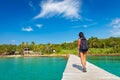 Young travel girl backpacker walks with backpack along a scenery wooden bridge to a tropical paradise island