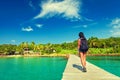 Young travel girl backpacker walks with backpack along a scenery wooden bridge to a tropical paradise island