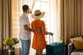 Traveler couple with luggage looking out of the hotel room window after arrival Royalty Free Stock Photo