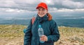 Caucasian young blonde girl shows water from plastic bottle. mountain background.