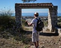 Young traveler guy stands with a map of the area in front of a stone destroyed gate, rear view