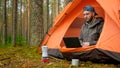 Young traveler guy talks to client via video link via laptop while sitting in nature in tent. Man talks to his boss on