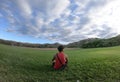 Young traveler male tourist sitting relaxing on a grass in front of mountains looking aside enjoying panoramic mountain in