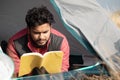 Young traveler reading book inside the tent by having some good time